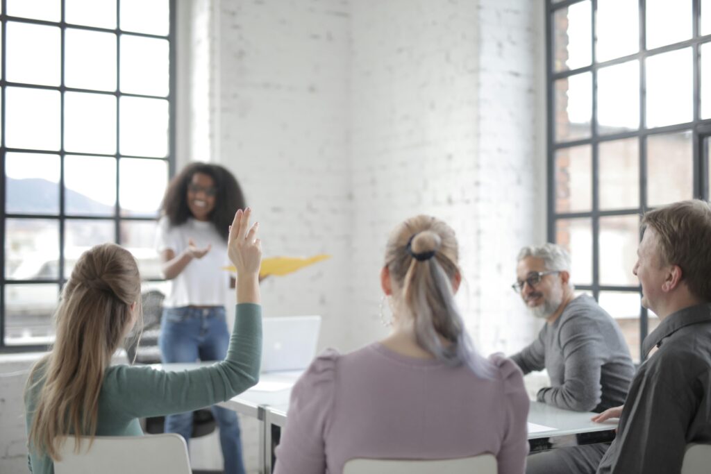 Female employee raising hand for asking question at conference in office boardroom